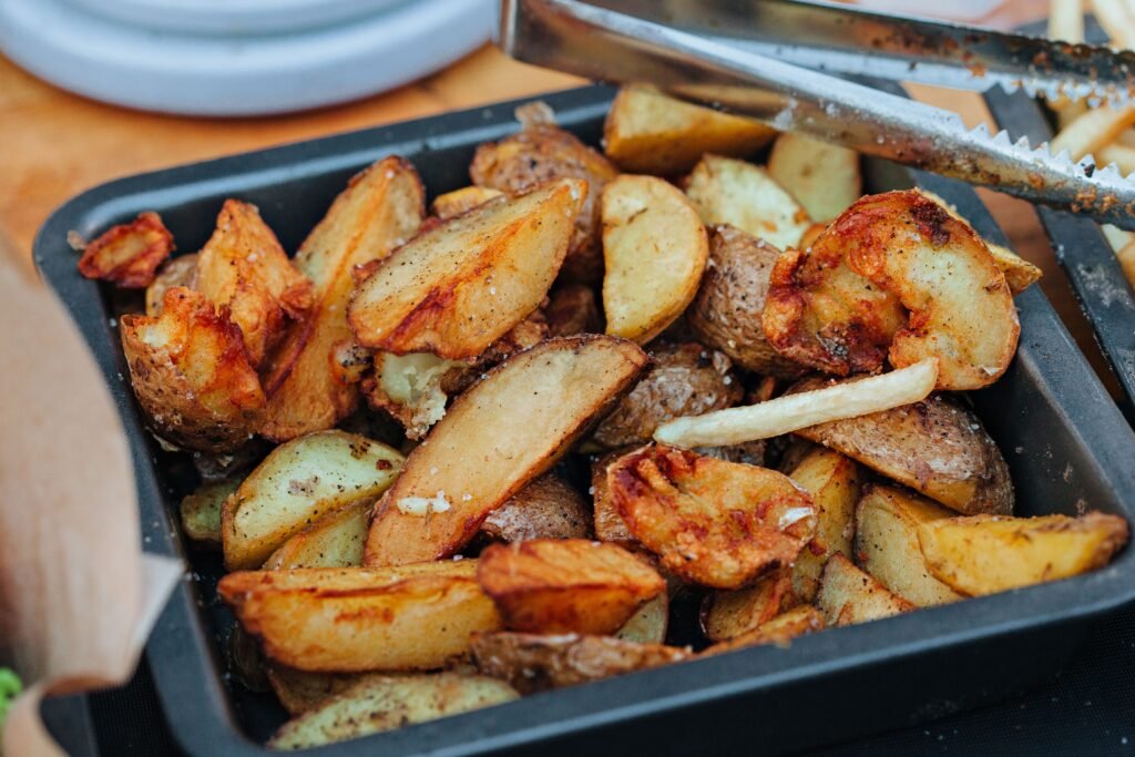 Batatas assadas douradas em uma forma escura, pegas com um pegador de metal