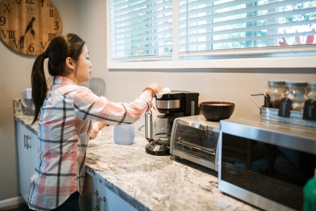 Mulher limpando cafeteira elétrica com pano na bancada da cozinha
